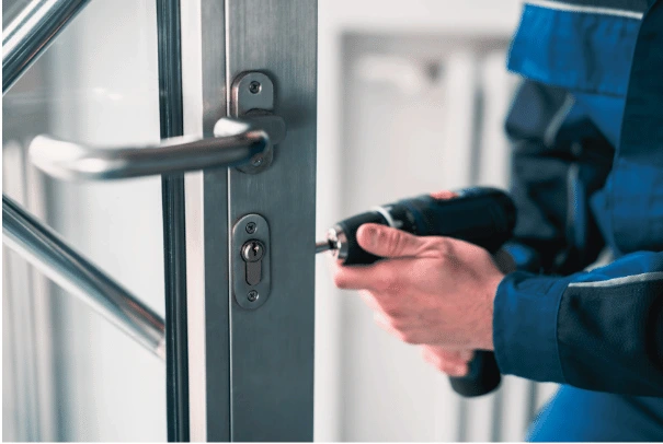 Technician fitting cylinder and lever hardware to an aluminium storefront door in a commercial building